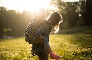 Older child giving a younger child a piggyback in a sunny field