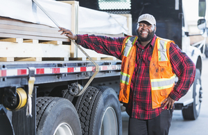 Timber trader in a high visibility jacket beside a truck loaded with wood. Credit: Getty Images