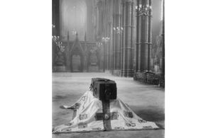 Black and white picture with a coffin laid in a church in the middle.