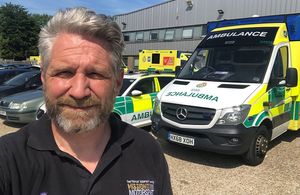 James Cameron standing in front of NHS ambulances smiling at the camera.