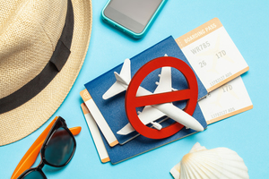 A beach hat, sunglasses and tickets on a table below a plane with a cancelled sign.