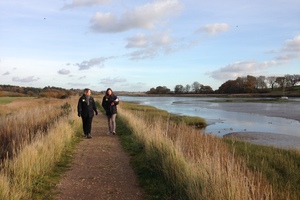 Two people in Natural England uniforms walking beside Martlesham Creek in Suffolk