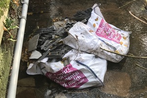 Two white builders' bags overflowing with corrugated strips of asbestos in a shallow stream