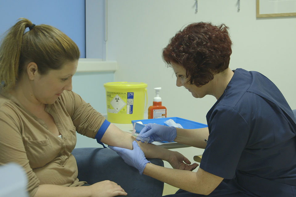 Sveikatos priežiūros specialistas paima kraujo mėginį iš moters rankos