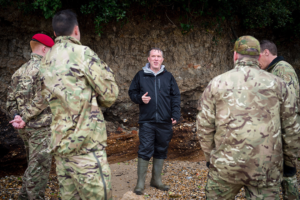 Richard Osgood talks to 4 soldiers in a rocky area of land.