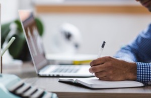 Image of note taking next to a laptop computer