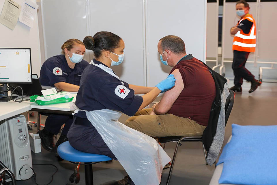 Image depicts a defence medic injecting a patron with a Covid-19 vaccine.