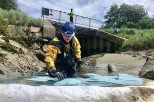 Image of an Environment Agency worker putting a floating barrier into place to trap oil on the surface