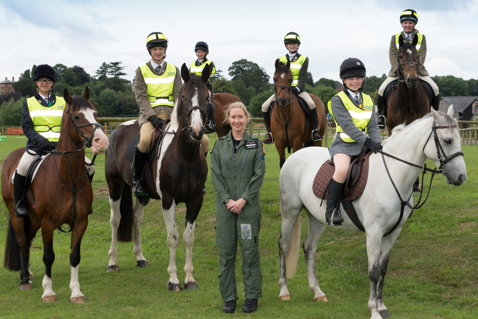 A member of aircrew from RAF Shawbury in full uniform standing next to members of the equestrian community on horseback. 