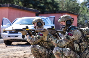 Royal Marines in camouflage crouch and point guns towards a target