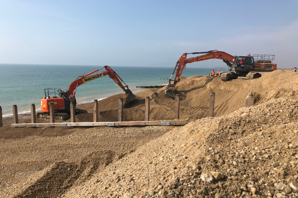 Image shows two excavators on top of a shingle bank overlooking the sea
