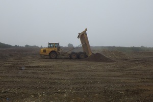 A flatbed truck dumps soil onto barren land