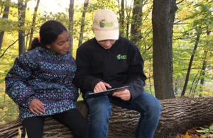 Two children sit on log, using Earth Rangers app on a tablet