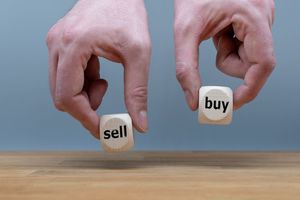Hands holding a pair of dice which read sell and buy
