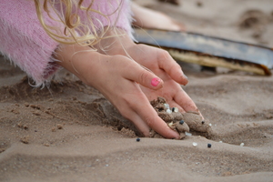 Girls hands holding sand on the beach which has plastic nurdles in it