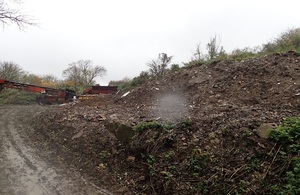 Image shows the edge of a dirt track to the left of the picture, curving round a large bank of earth, beyond which can be seen some heavy machinery