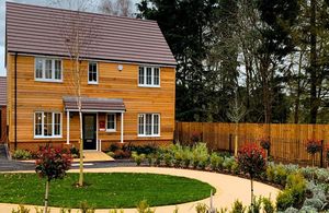 A photo of a house covered in wooden panelling, surrounded by trees and shrubs