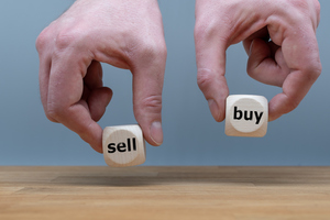 Руки держат два кубика со словами "продать" и "купить"