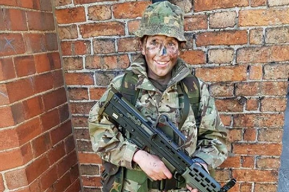 Cerys in camo uniform holding a large gun. 