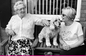 A black and white image of two people sitting on a bench with a dog in the middle