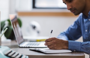 Man making notes while working on laptop