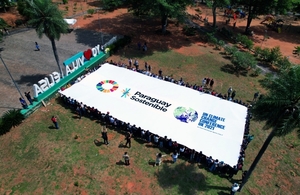Young climate activists wave a giant flag with the logo of the Sustainable Development Goals and the phrase "Paraguay Present at COP26".