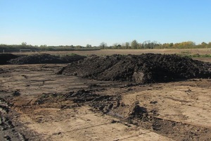 Large pile of dry sewage sludge lying on the ground near a field