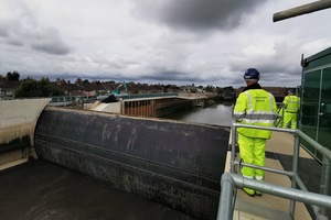 Environment Agency man in high-visibility clothes and hard hat looks down into a waterway where the barrier gate is raised.