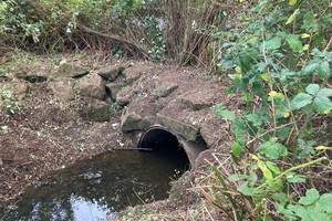 A small tunnel under a bank, with water running through it