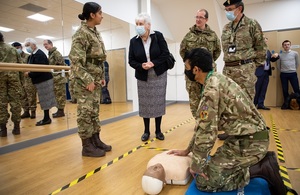 Baroness Goldie stands with three cadets in uniform while a fourth cadet is knelt on the floor demonstrating how to perform CPR