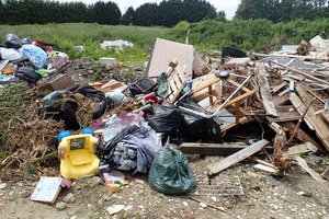 Rubbish heaped into a pile on open land, including wood, plastic toys, black bags and vegetation
