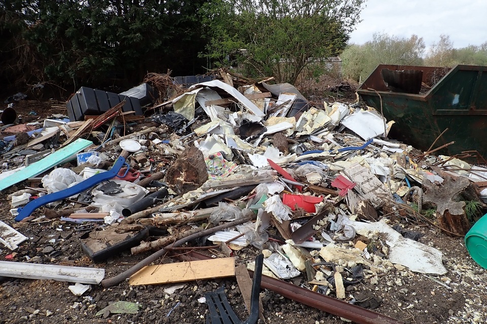 A heap of wooden planks, paper, plastic and other rubbish on the ground next to a skip