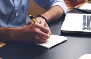 Man with laptop making notes on paper pad