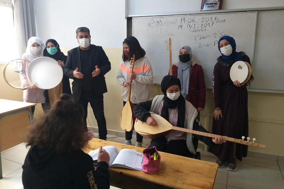 A teacher and several young girls stand before a whiteboard. The girls are holding a range of traditional instruments.
