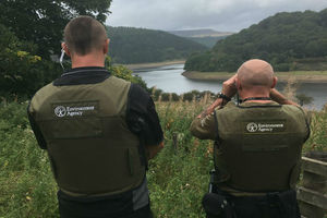 The backs of 2 fisheries officers looking through binoculars at a river