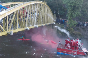 Bridge over river where there is a raft being pelted with bags of flour