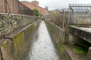 Straight water channel with concrete walls either site and buildings in the background