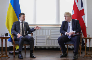 Boris Johnson and Volodymyr Zelenskyy sitting beneath UK and Ukrainian flags.