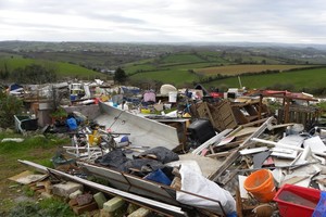 Rubbish including doors, buckets, furniture and other waste scattered in foreground with green hills in background