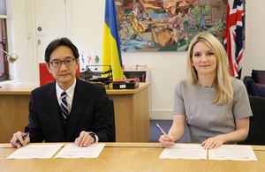 Minister Sasaki (left) sitting with Minister Lopez (right), both signing a document