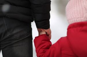Child in pink hat and red coat holding hands with adult in black coat