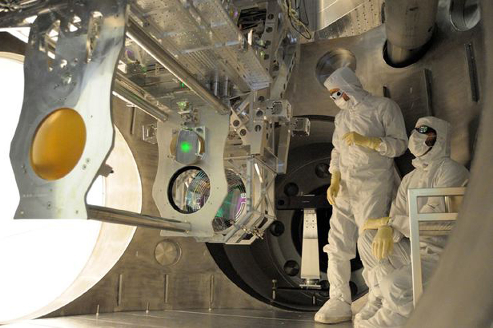 People in protective clothing inside a large machine full of scientific equipment.