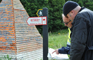 Two men looking at paper work next to rights of way signs on Salisbury Plain Training Area.