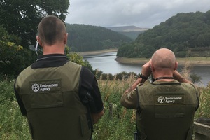Two Environment Agency officers checking a distant riverbank using binoculars