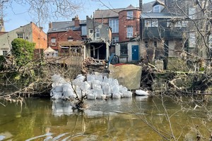 White bags containing rocks, on the river bank in front of several houses
