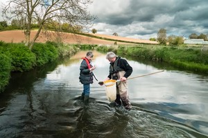 Man and woman in waders looking at a big net holding a sample taken from a river bed