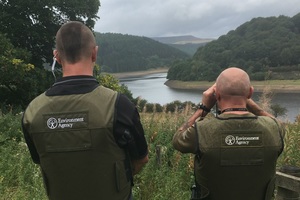 The back of 2 Environment Agency offers looking through binoculars at a river in the distance