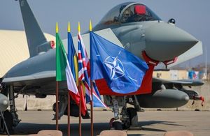 An RAF Typhoon on the tarmac in Romania. The Italian, Romanian, UK and NATO flags fly in the foreground.