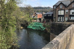 Green bags of rocks piled up against a river back in front of houses