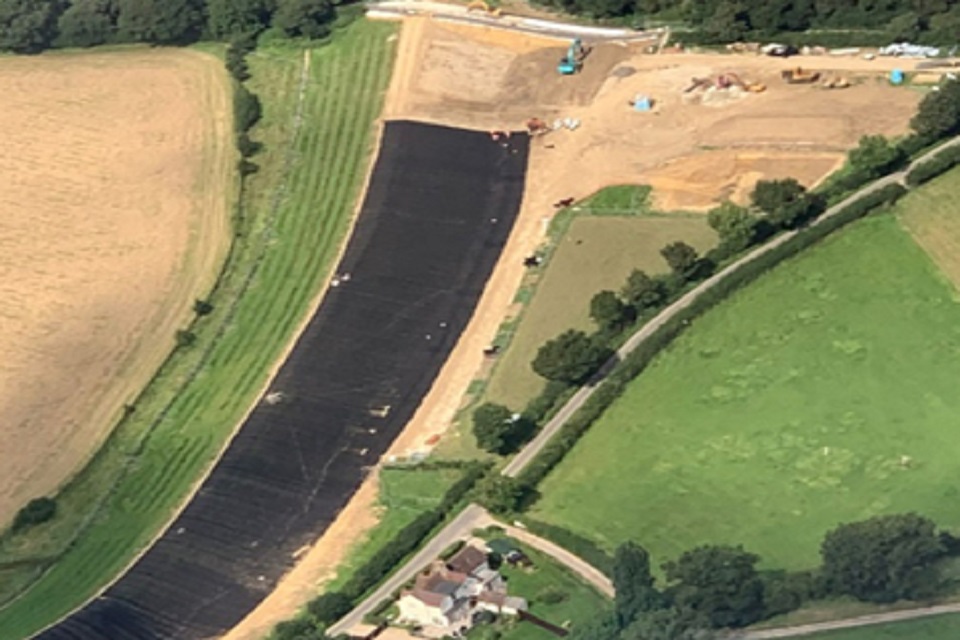Aerial view of site showing large strip of black matting extending upwards between green fields. Earthworks can be seen at the top.
